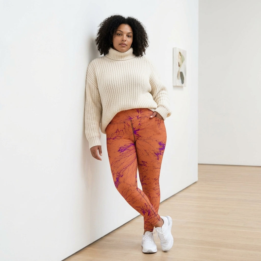 Model leaning against a white wall wearing Admire Orange Purple Wing leggings.